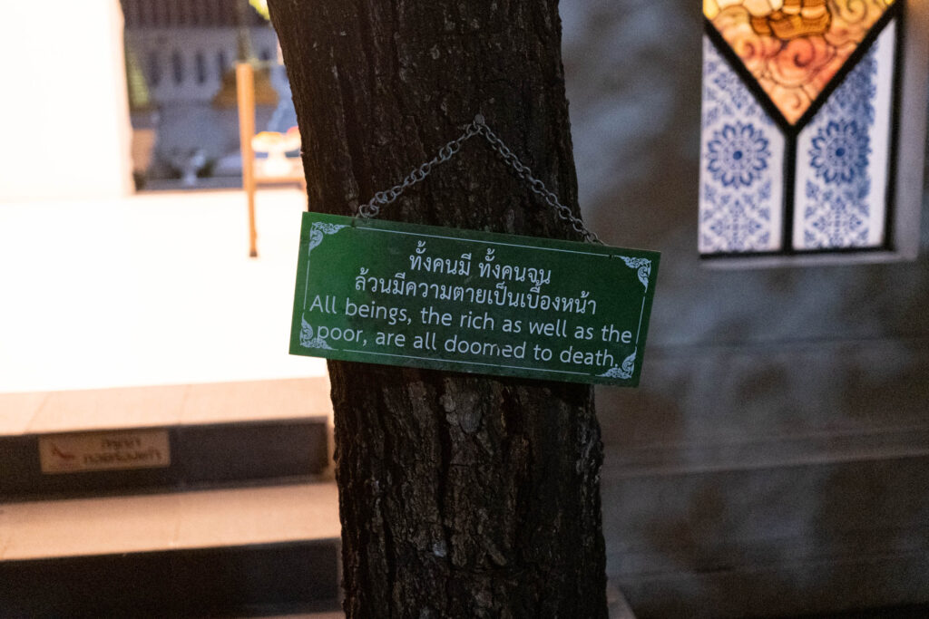A sign at a tree, inside a buddhist temple in Chiang Mai: "All beings, the rich as well as the poor, are all doomed to death."