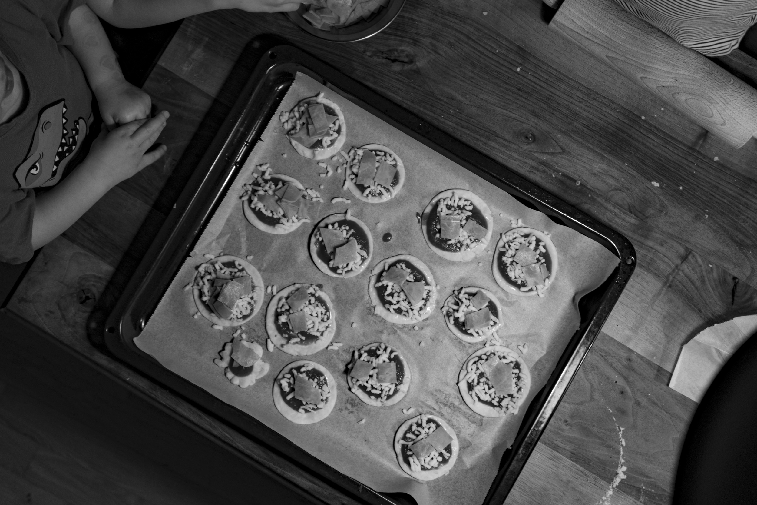 A tray full of mini pizzas, pictured from above in black and white.