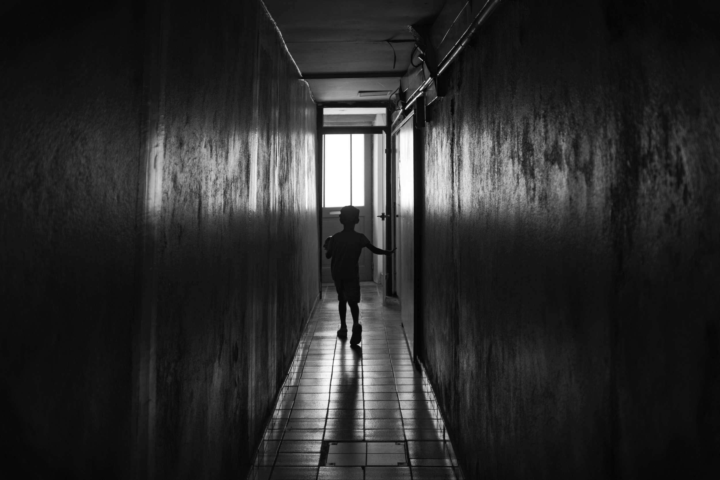 A black and white shot of our young one from behind, walking out the long, dramatically lit hallway leading to our apartment in La Rochelle.