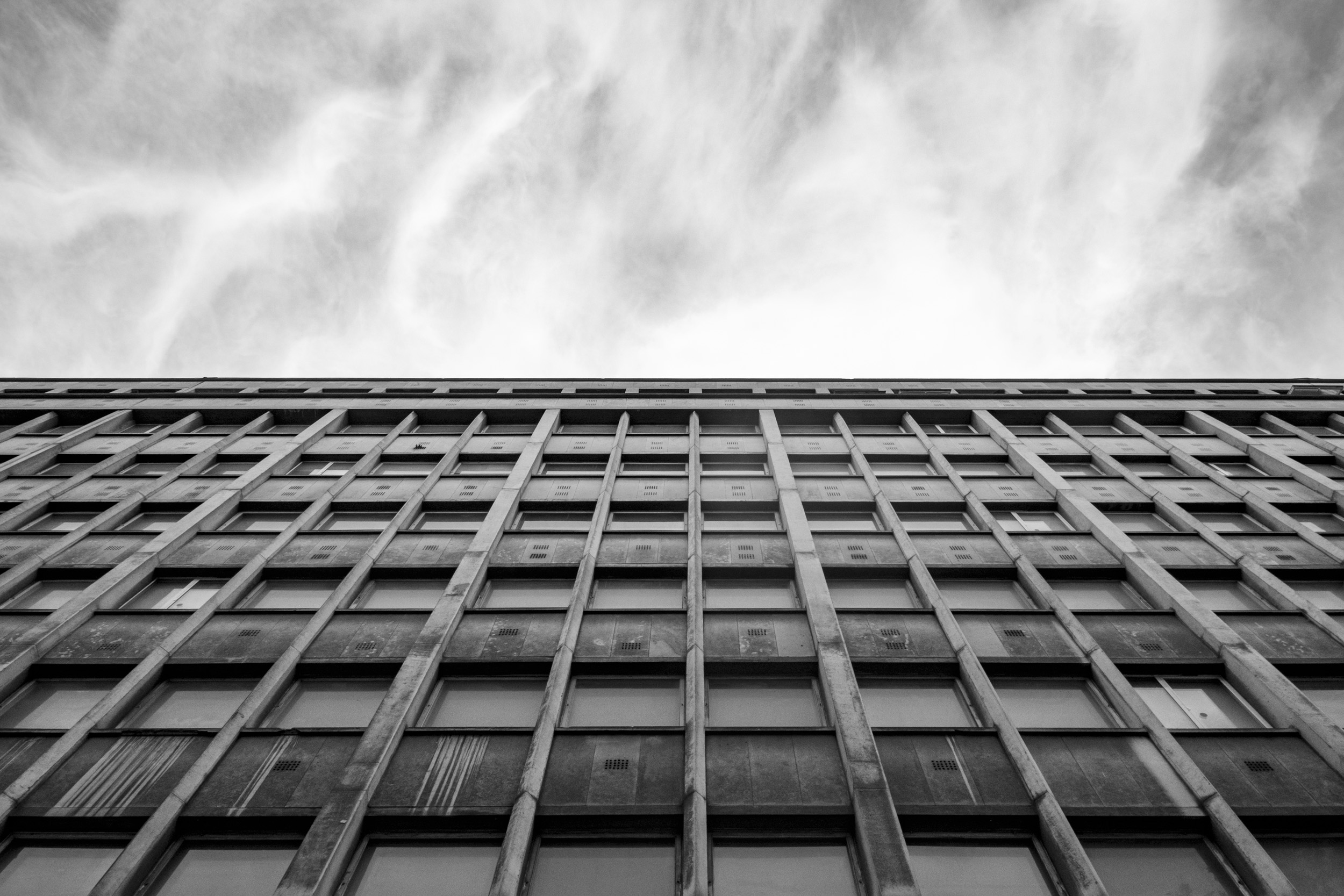 Low-angle black-and-white photo looking up the concrete grid facade of the former Faculté des Sciences in Paris, against a cloudy sky.