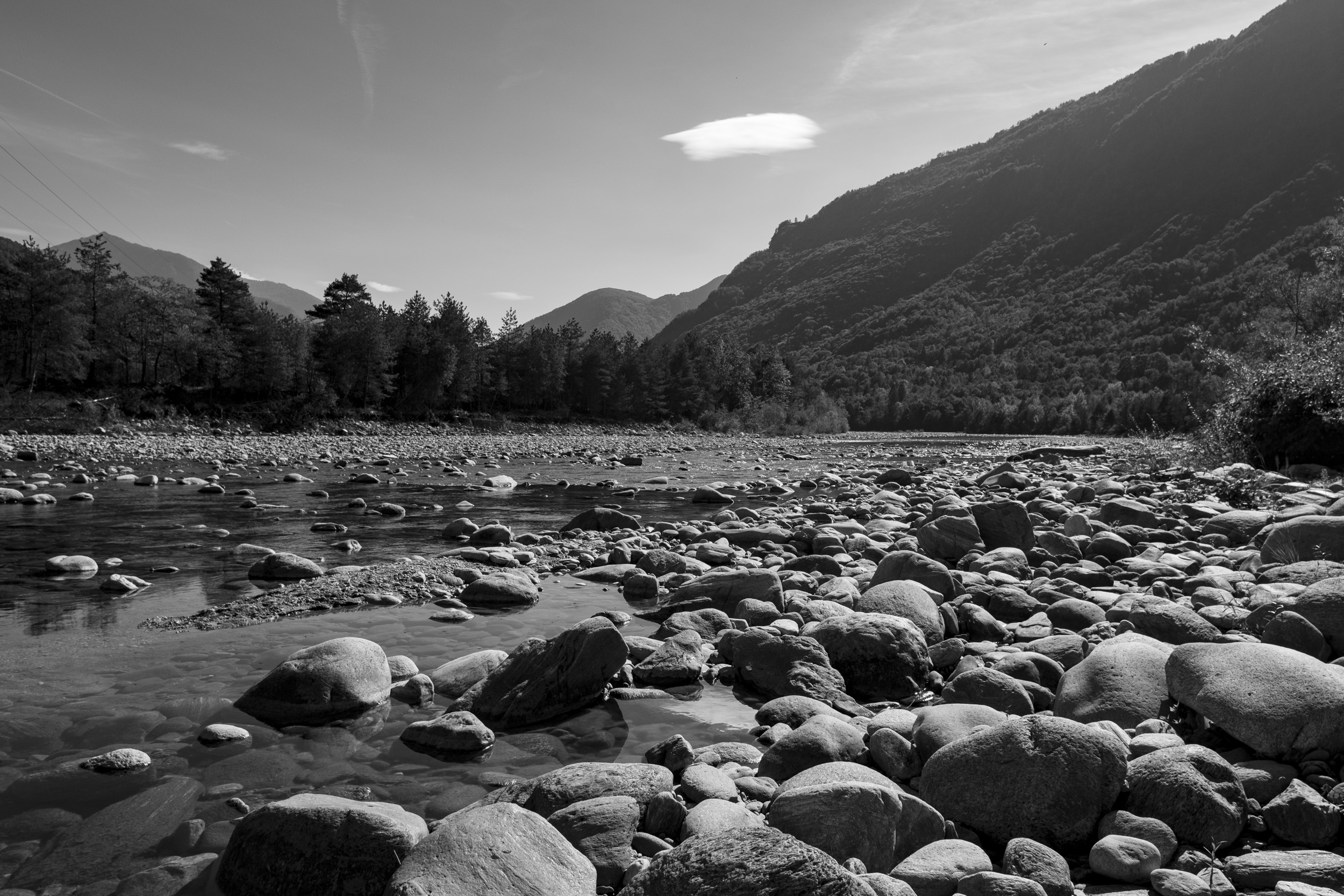 Black-and-white photo of the Maggia River in Ticino after a dry summer, its riverbed mostly exposed stones with only shallow pools of water.